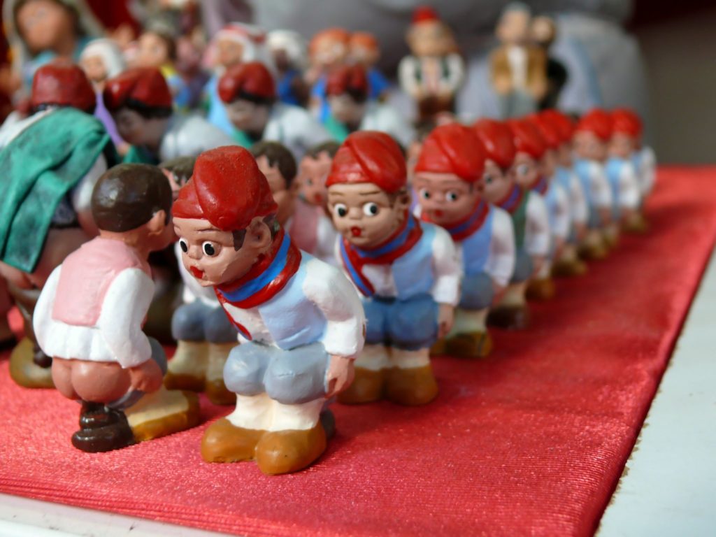 A photograph of rows of small figurines wearing red hats. They are crouching with their trousers pulled down.